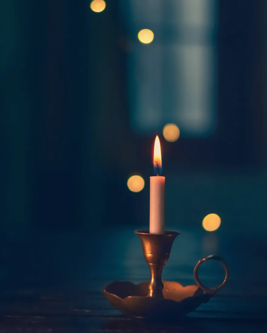 Bougie allumée sur un chandelier, petites lumières floues dans un décor bleu sombre