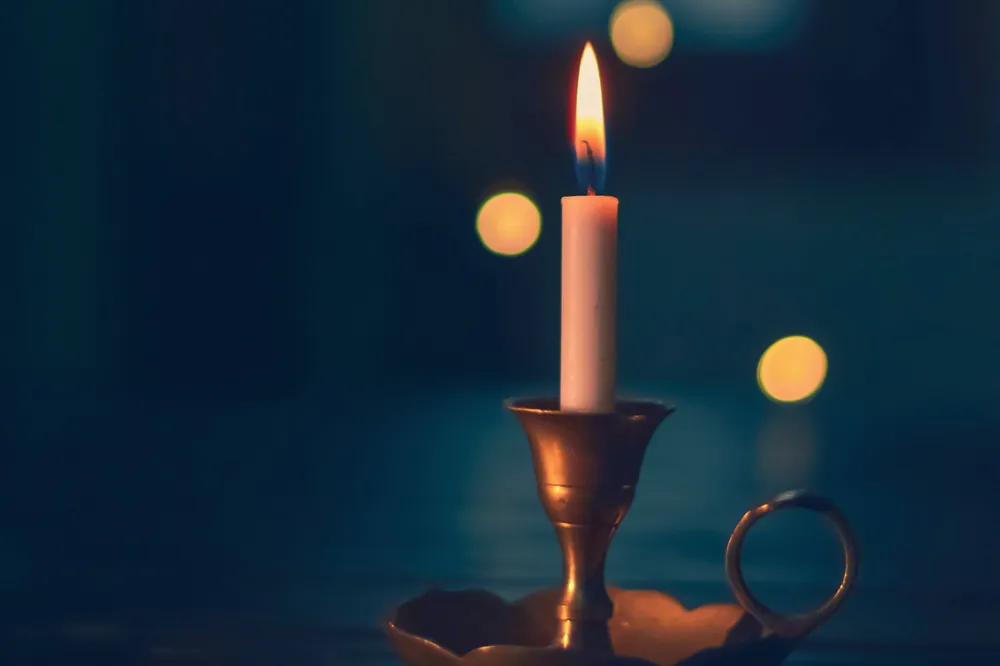 Bougie allumée sur un chandelier, petites lumières floues dans un décor bleu sombre