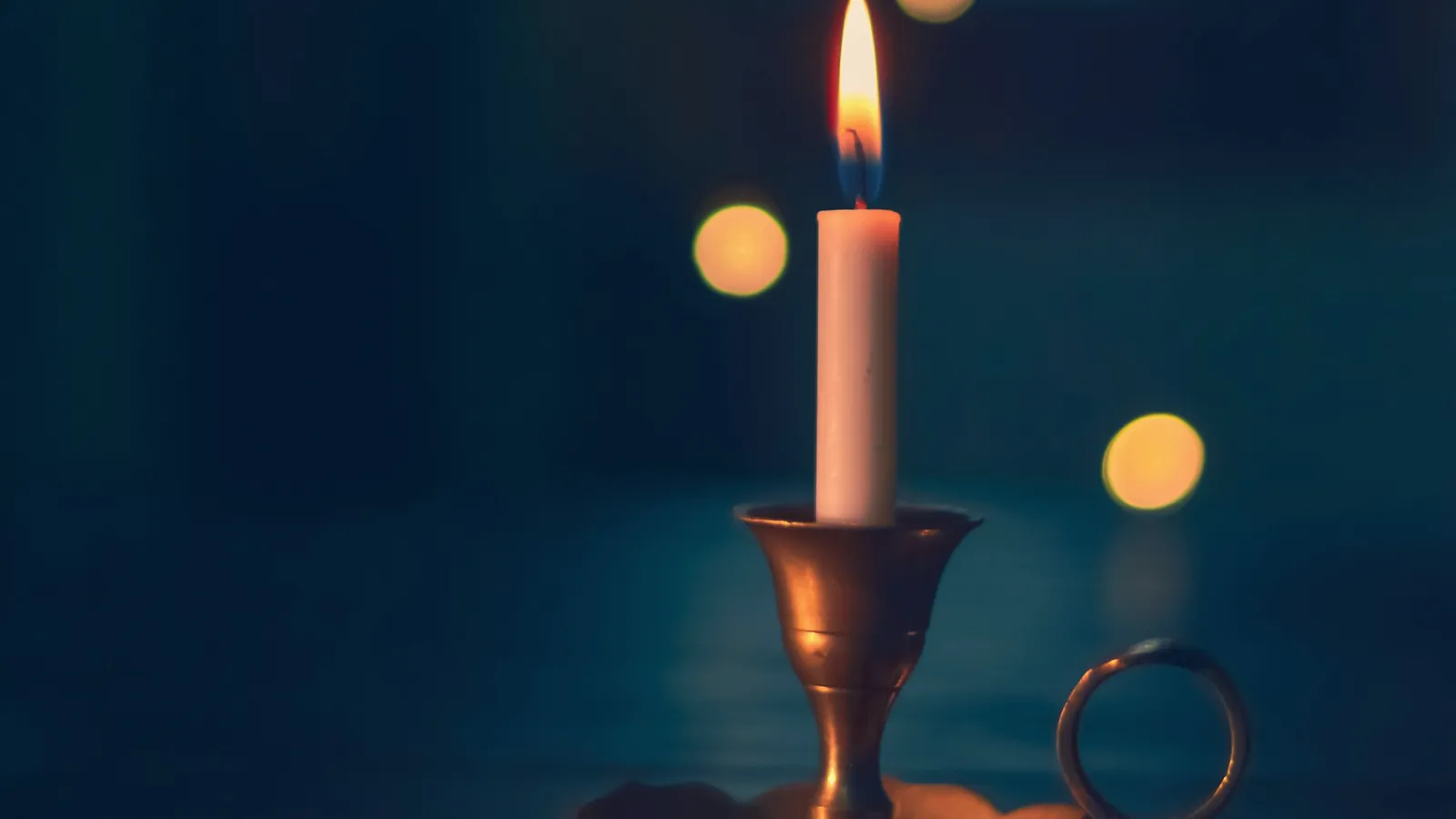 Bougie allumée sur un chandelier, petites lumières floues dans un décor bleu sombre