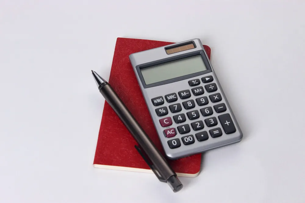 Calculatrice posée sur un carnet rouge, à côté d’un stylo