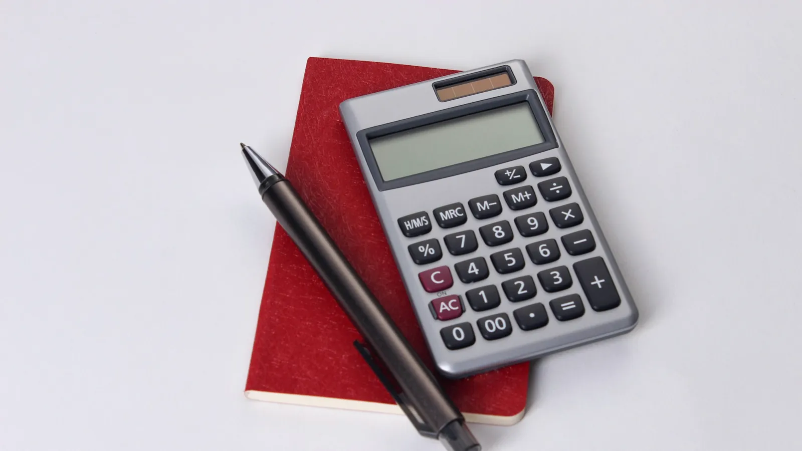 Calculatrice posée sur un carnet rouge, à côté d’un stylo