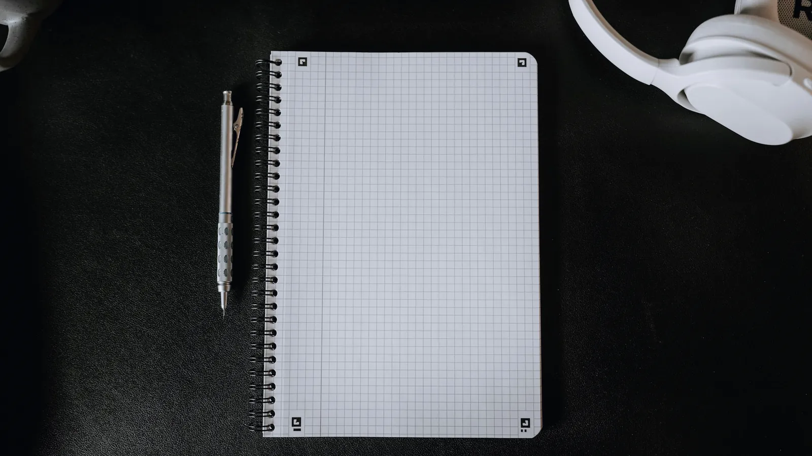 Carnet à spirale, stylo à bille et casque audio blanc sur un bureau noir