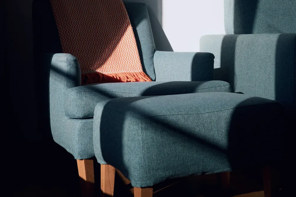 Deux fauteuils bleu sombre garnis d’un plaid orangé, dans une pièce traversée d’un rayon de soleil