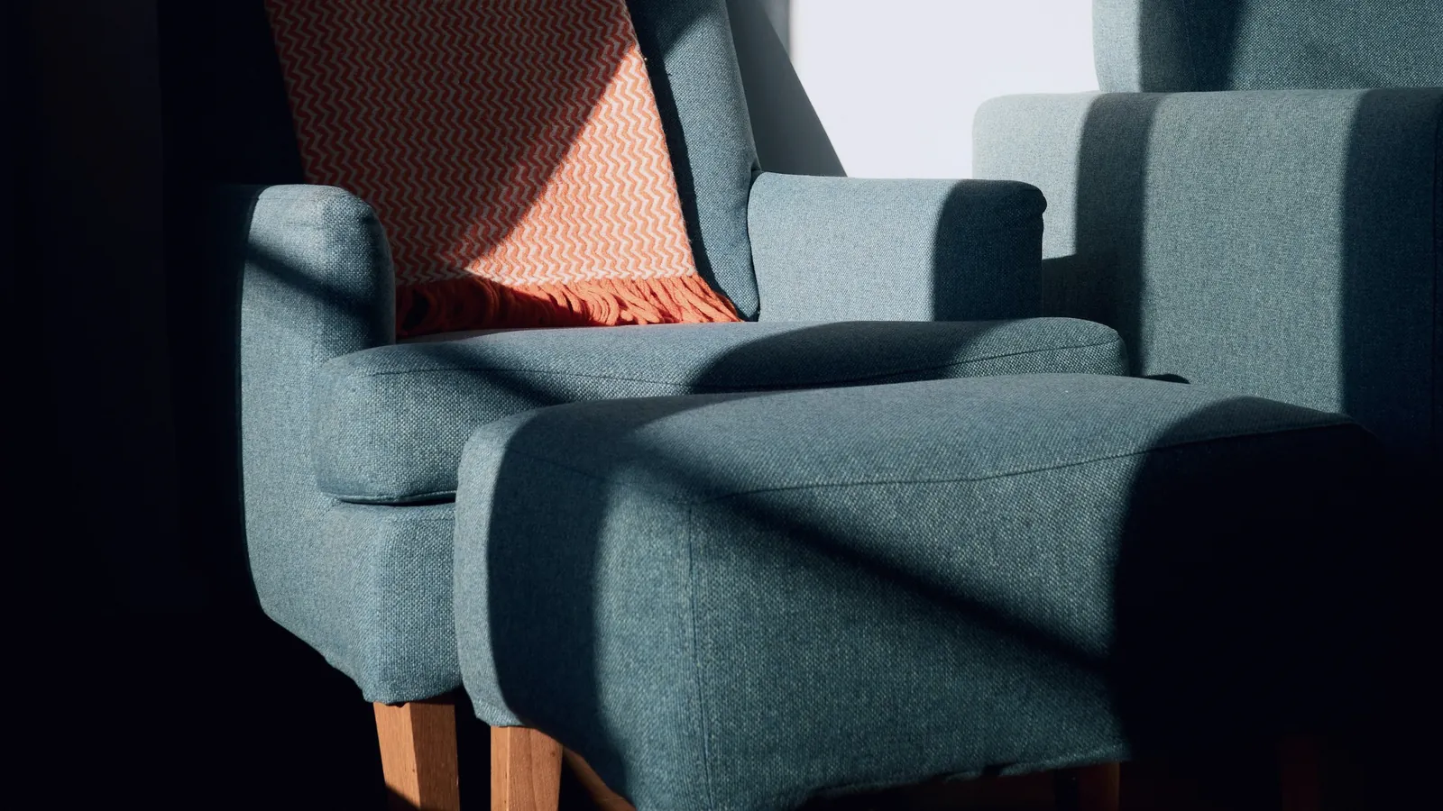 Deux fauteuils bleu sombre garnis d’un plaid orangé, dans une pièce traversée d’un rayon de soleil