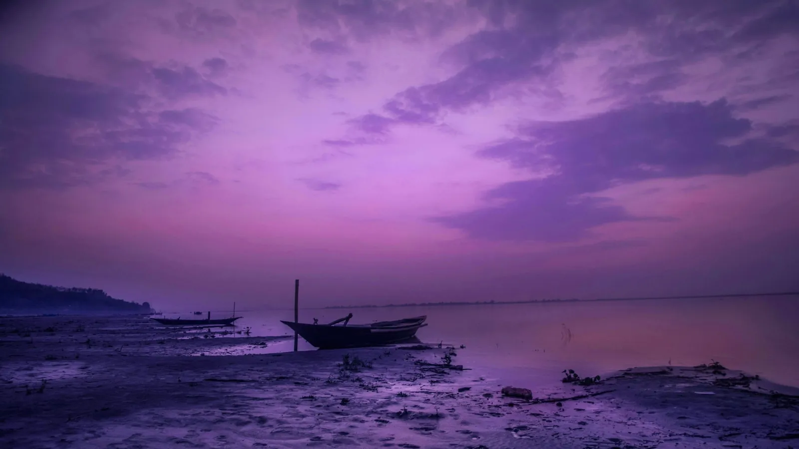 Ciel violet chargé de nuages au-dessus d’une barque échouée sur la grève