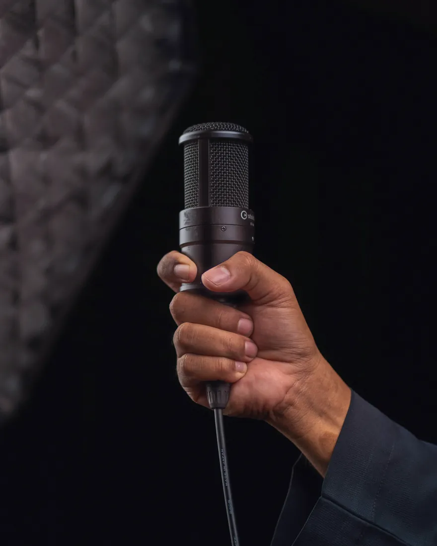 Une main tient un micro à condensateur devant un fond sombre capitonné