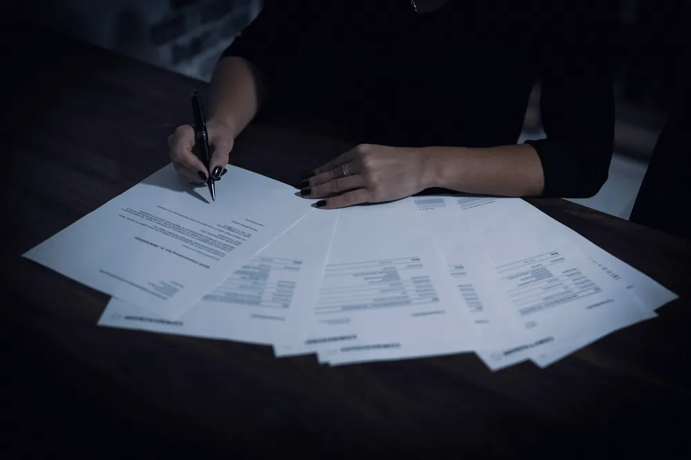 Mains qui signent des feuillets étalés sur une table sombre