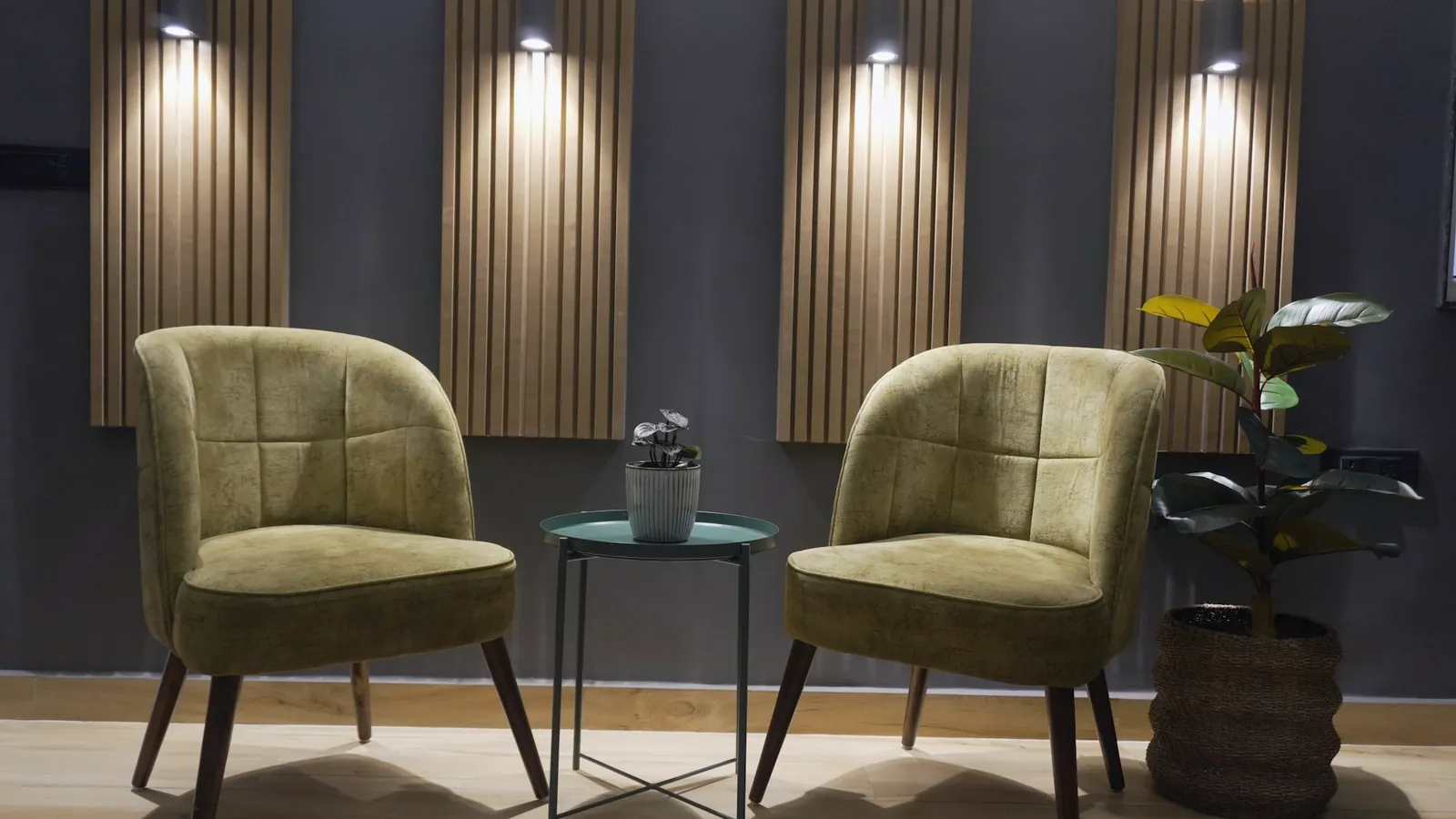 Petite salle d’attente aux panneaux de bois sombre, deux fauteuils verts et une plante