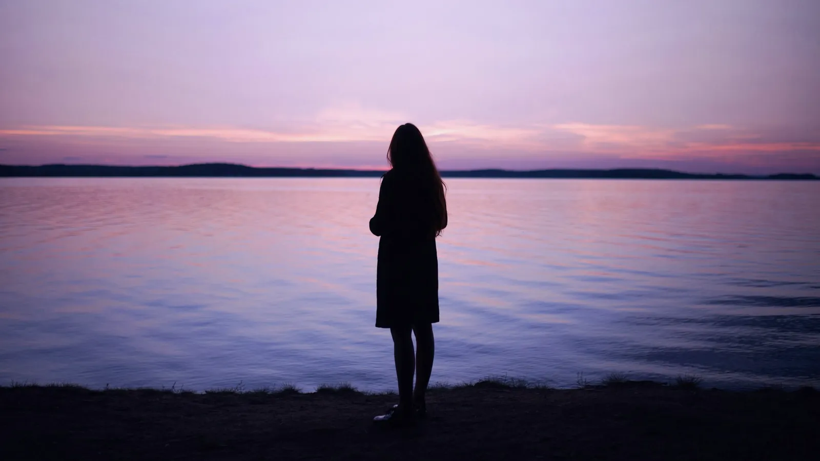 Silhouette vue de dos au bord d’un lac, sous un ciel rosé du soir