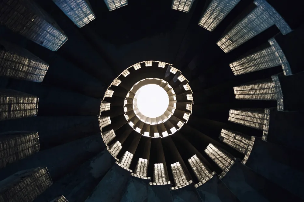 Escalier en colimaçon vu d’en bas, marches qui se resserrent en spirale vers une ouverture claire