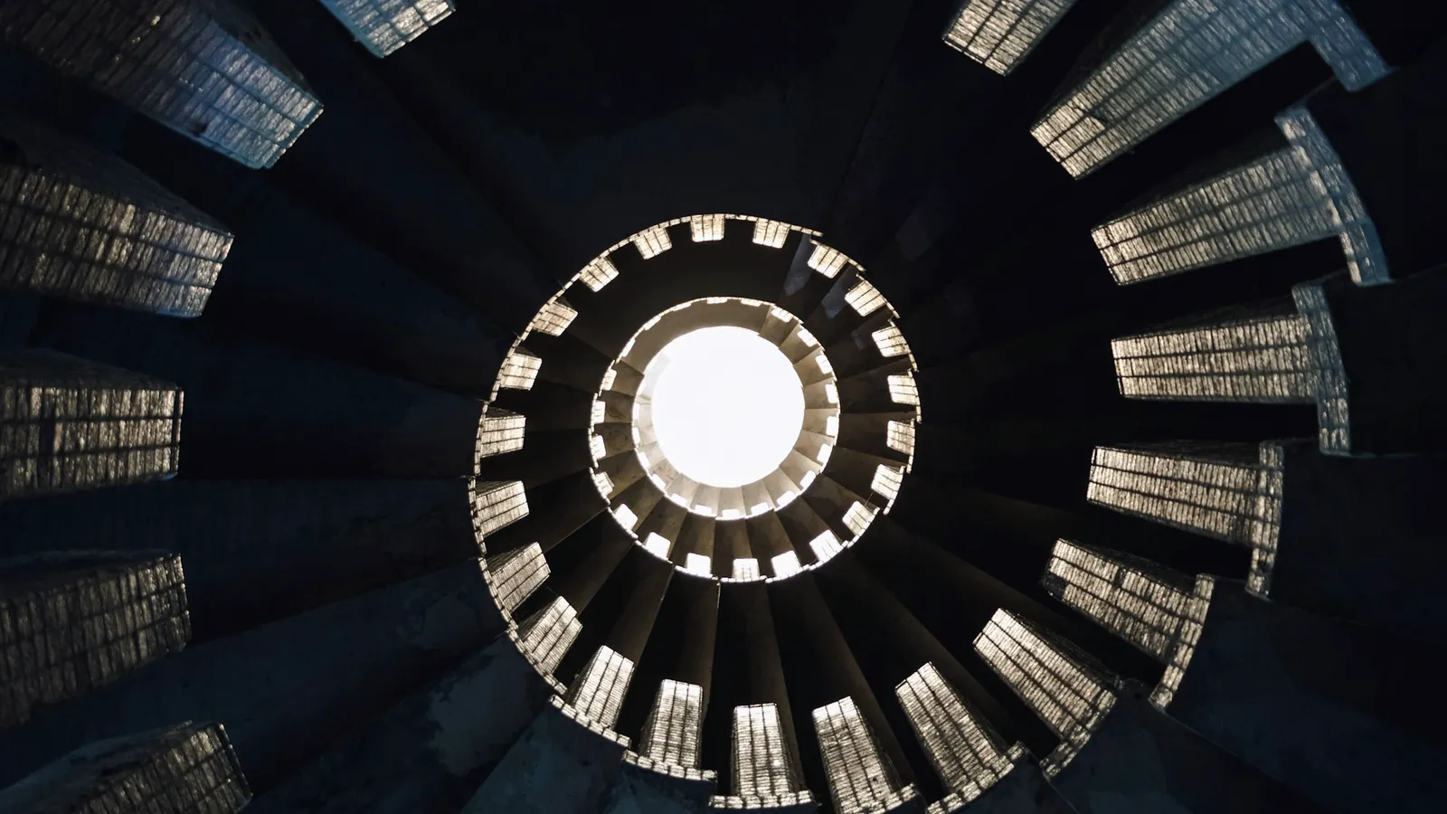 Escalier en colimaçon vu d’en bas, marches qui se resserrent en spirale vers une ouverture claire